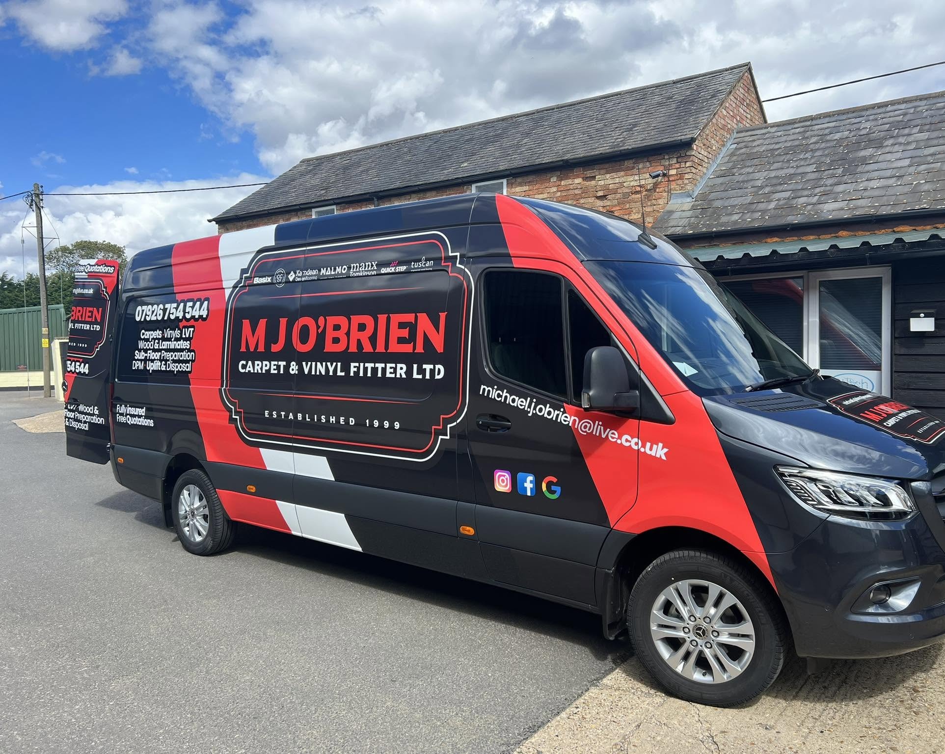 The M J O’Brien van in black and red livery, parked outside a brick building