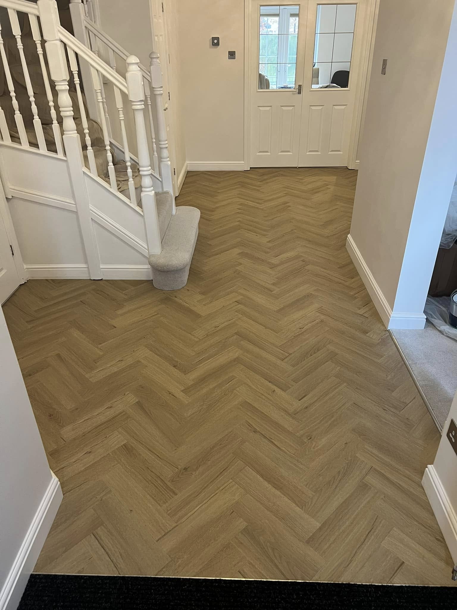 Honey oak herringbone floor in a hallway at the foot of a white staircase