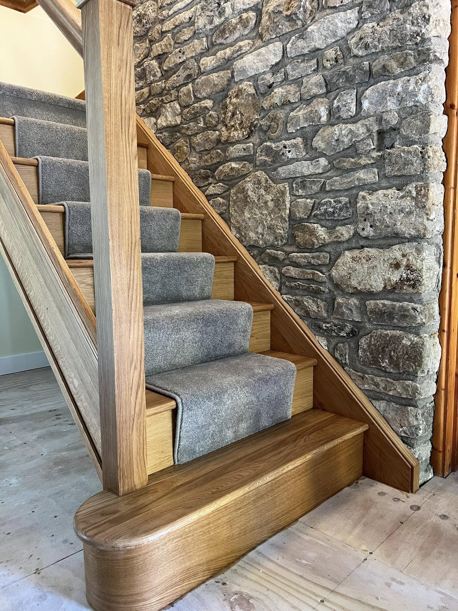 Grey stair runner on oak stairs beside an exposed stone wall