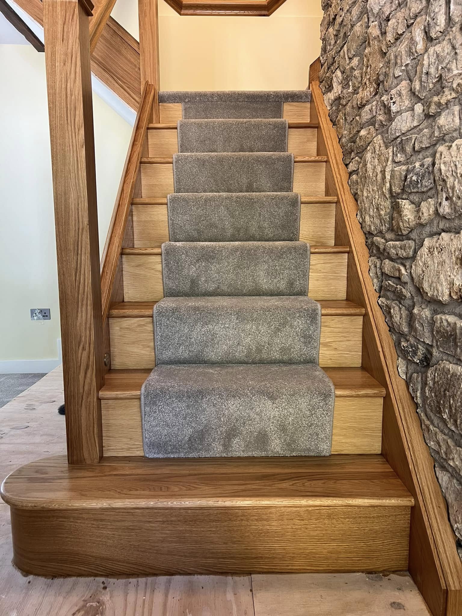 A full flight of oak stairs with a grey runner beside an exposed stone wall