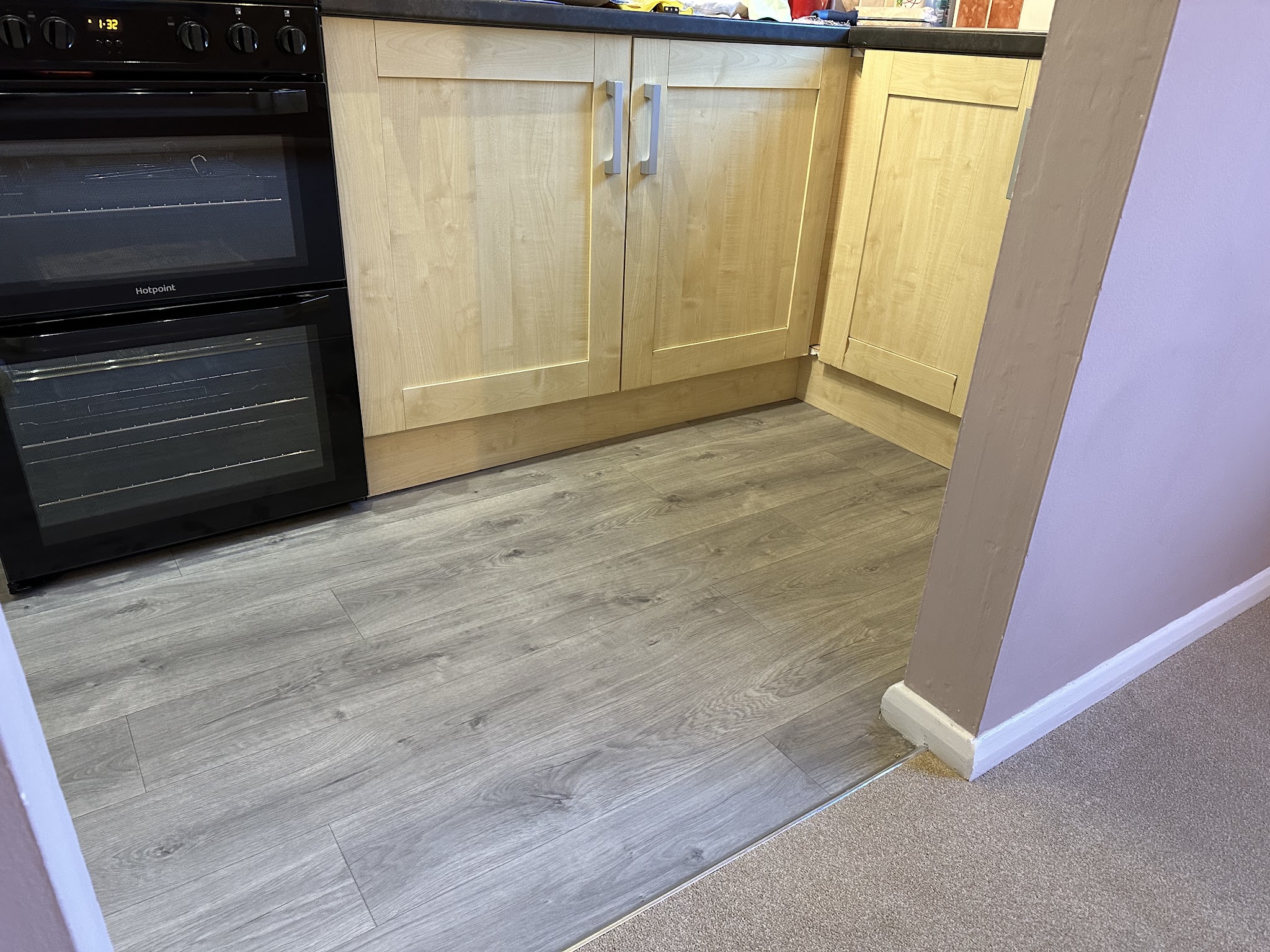 Grey wood-effect floor in a kitchen meeting carpet at the doorway